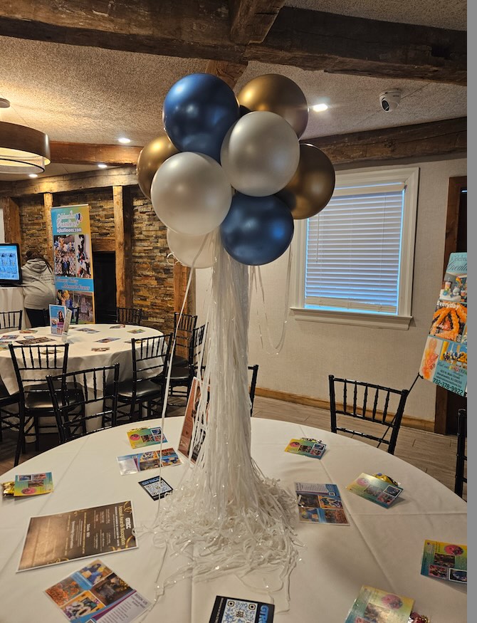 Elegant balloon centerpiece by Celebration Creations in Bayville, NJ, featuring clusters of metallic blue, gold, and pearl white balloons with cascading white ribbon, designed for a local business networking event.