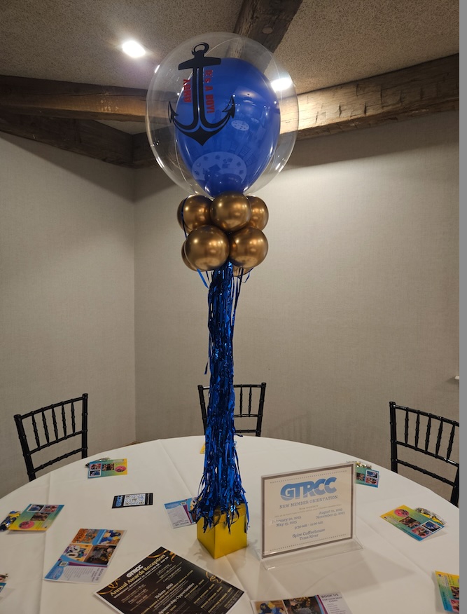 Custom nautical-themed balloon centerpiece by Celebration Creations at a Greater Toms River Chamber of Commerce event, featuring a blue anchor-printed balloon inside a clear bubble balloon, accented with gold balloons and blue metallic streamers.